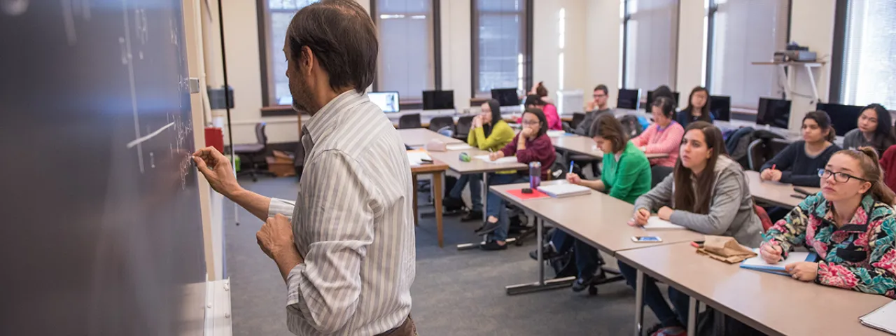 Pau Atela writes math problems on blackboard to classroom of Smith College students