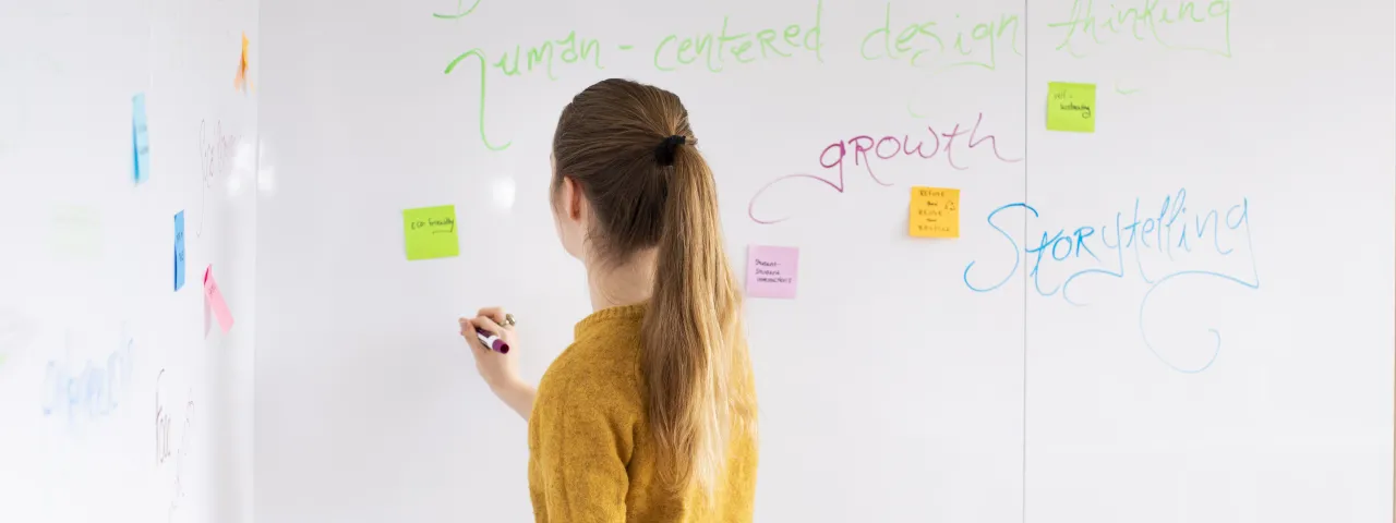 A student stands at a white board, writing.