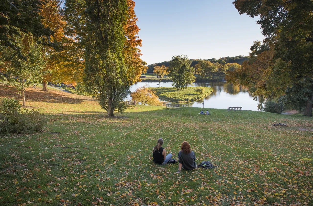 Two students sitting in front of Paradise Pond in the fall.