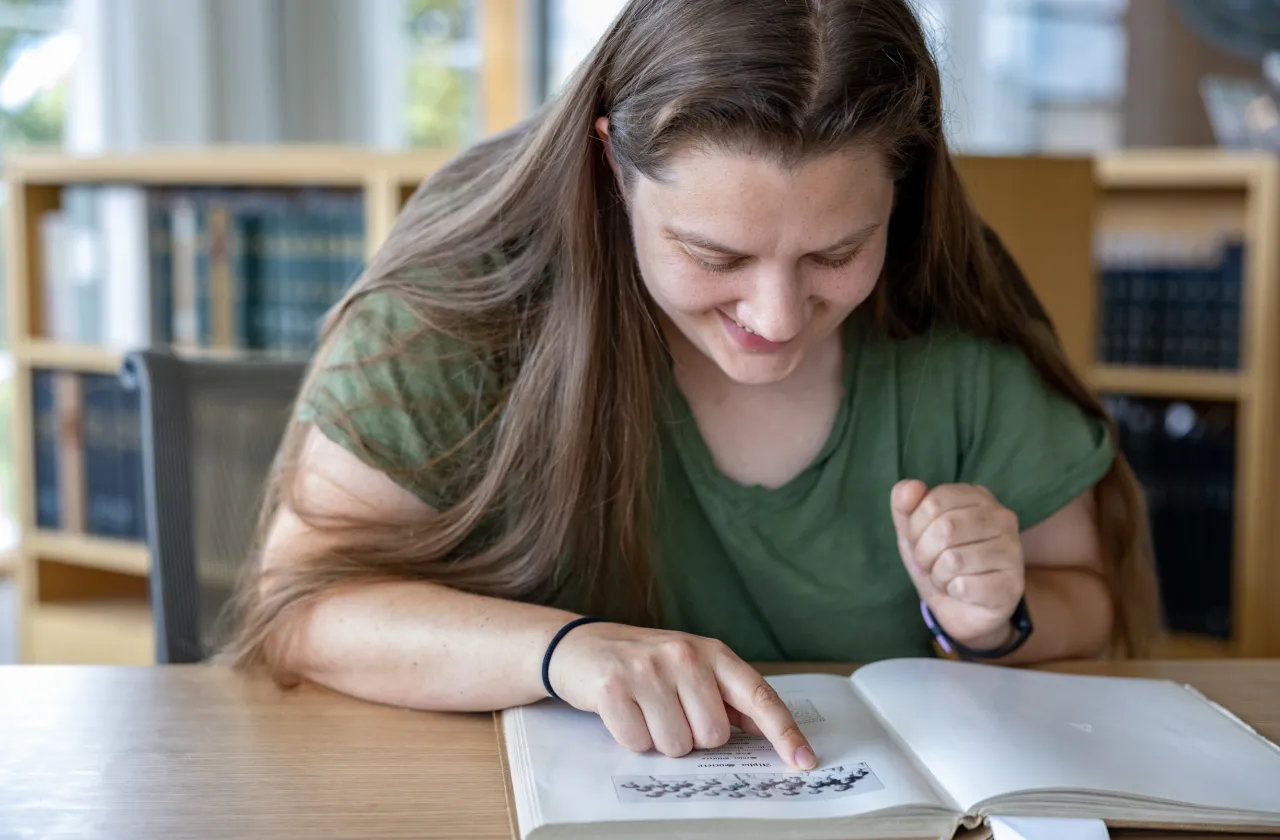 Kady Wilson smiles while looking at an old yearbook in Special Collections