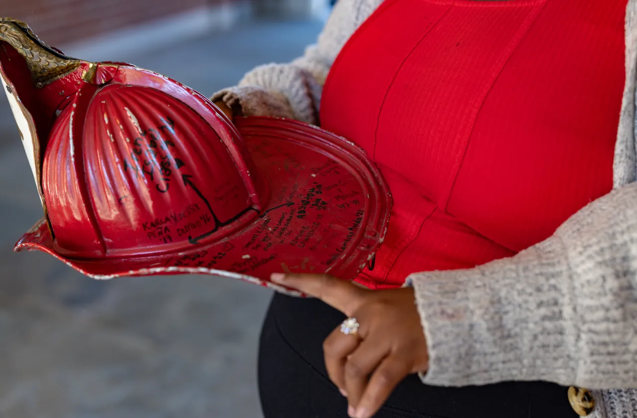 Diamond Jones' hand pointing to names on the red Comstock fire helmet