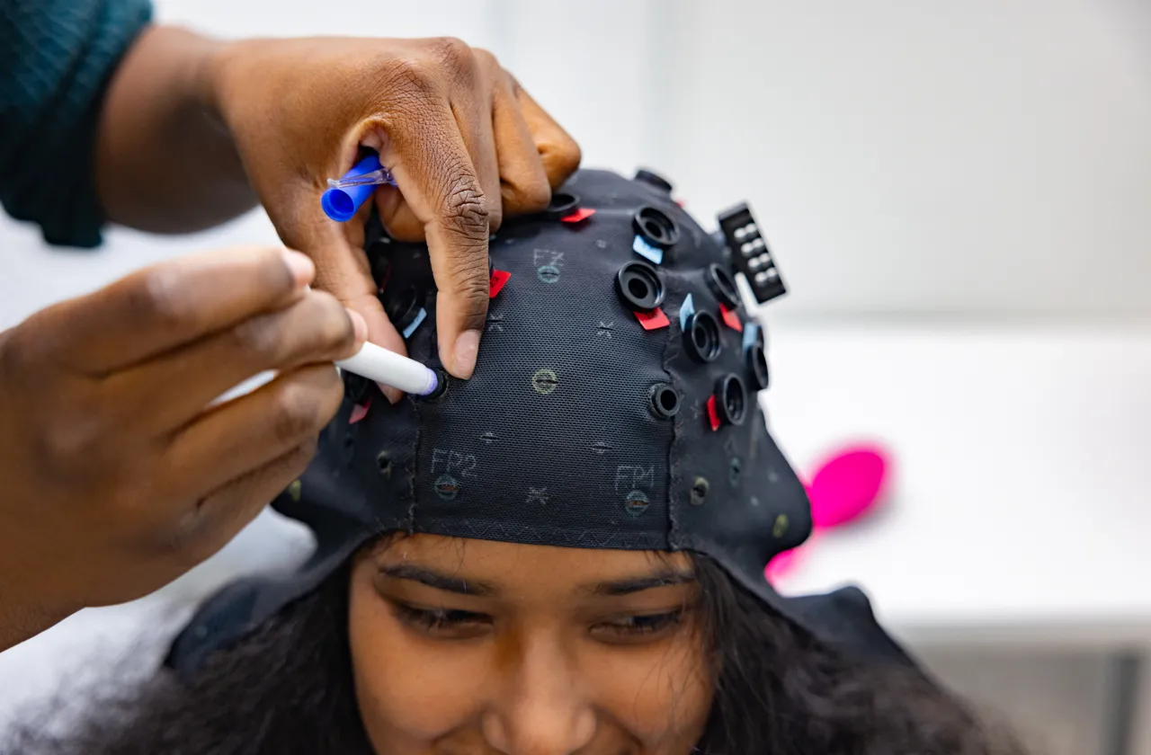 Student researcher Kris Cheaye fits an fNIRS cap to Gloriamar Esteves’s head