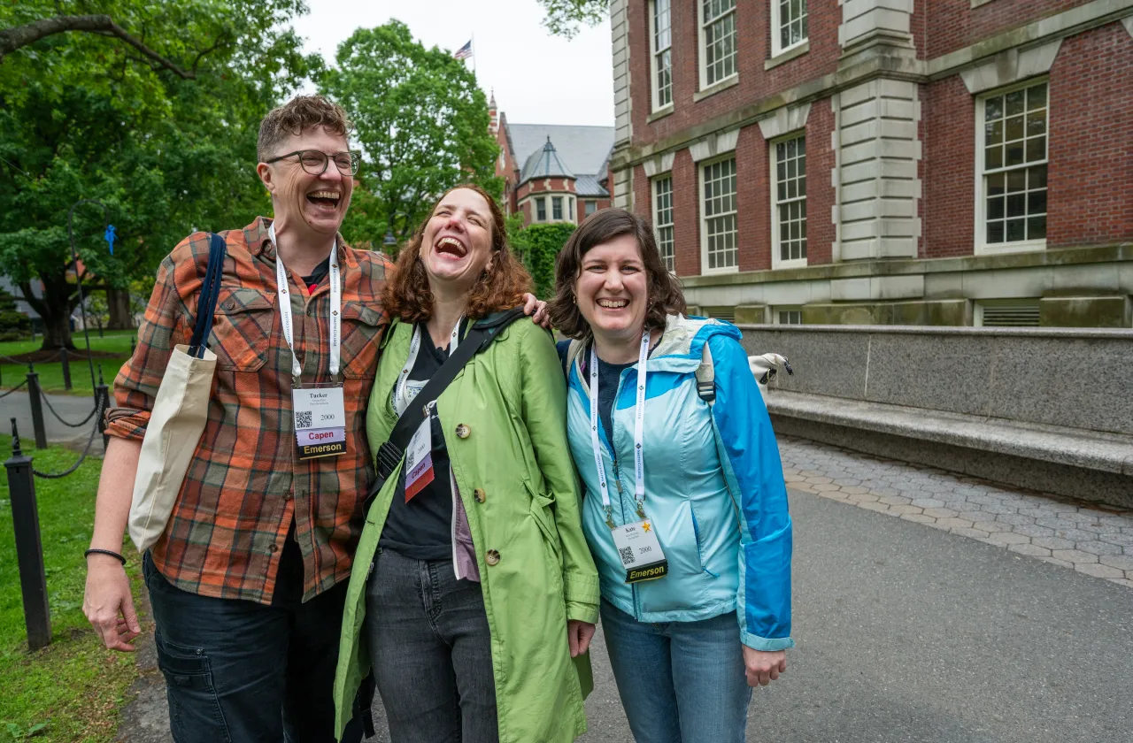 Three alums stand in front of Seelye Hall, laughing