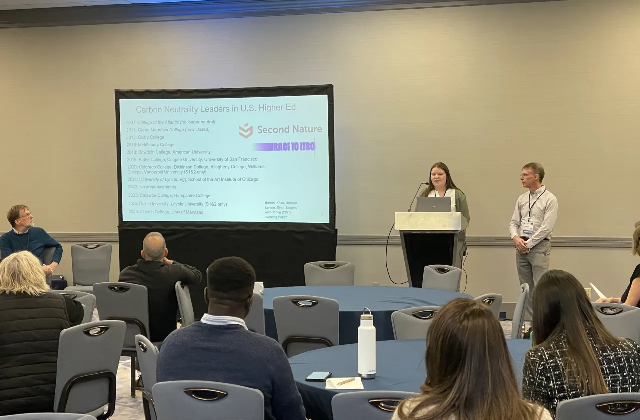 Emma Larsen presents research to a group while Alex Barron looks on.