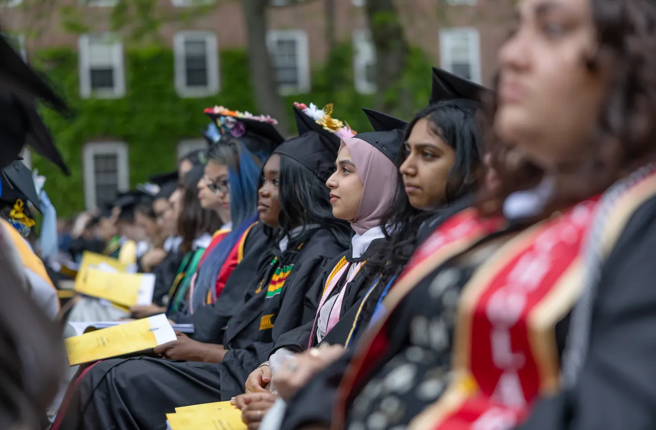 Students in caps and gowns sit in a row at Commencement.