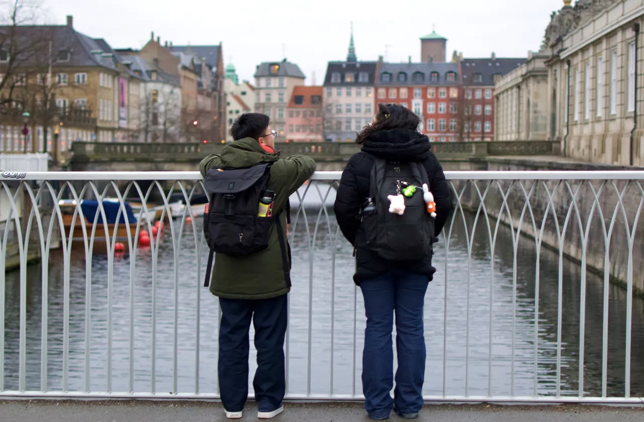 Two students stand on a bridge in Europe and look at the water below.
