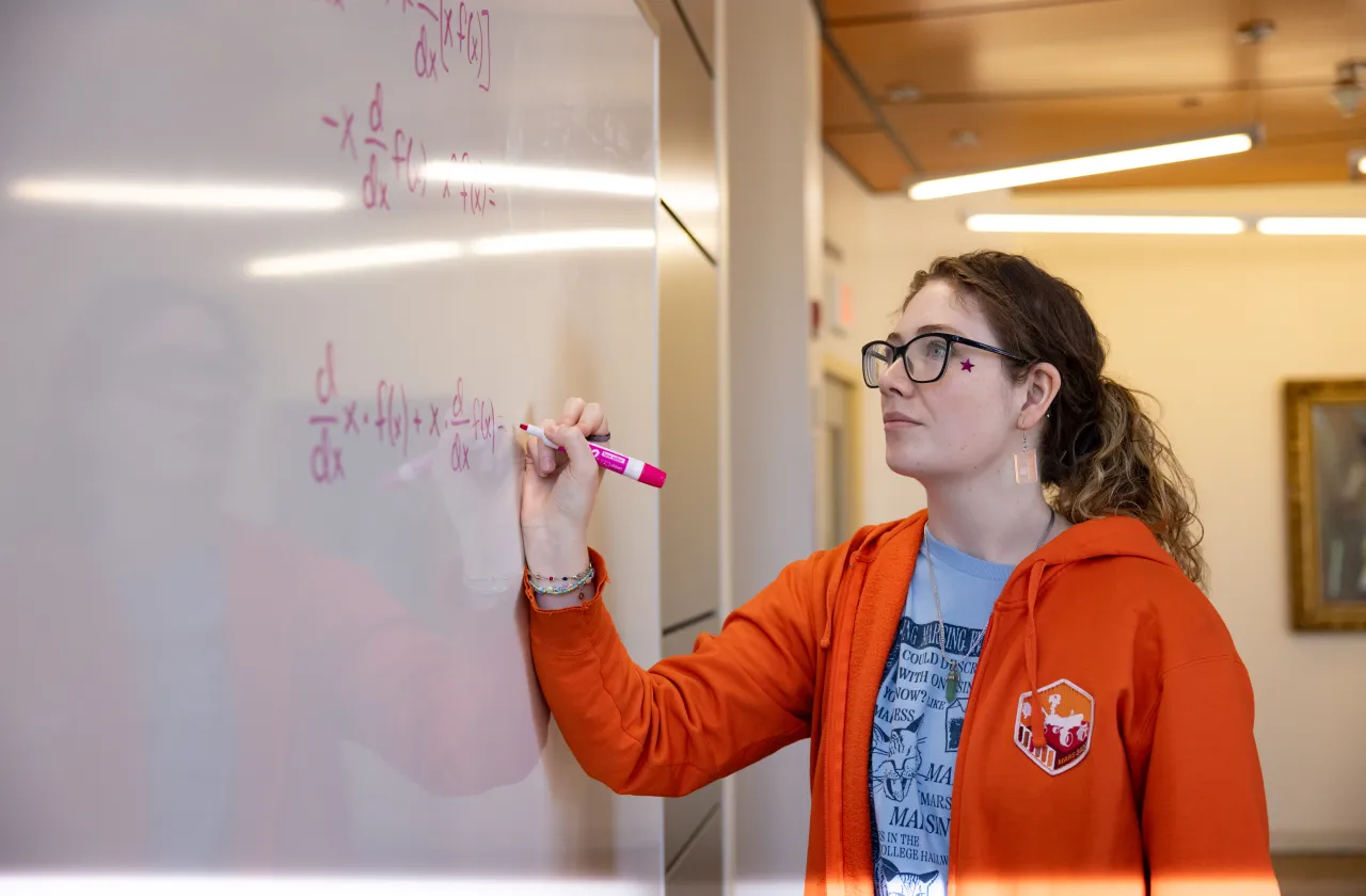 A student writes a math equation on a whiteboard. 