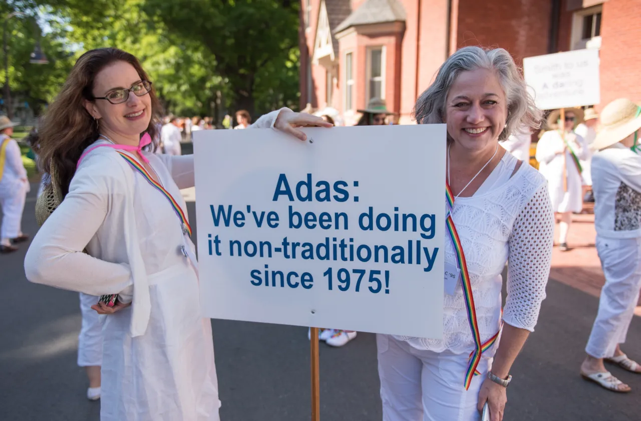 Two alumnae with sign "Adas have been doing it non-traditionally since 1975"