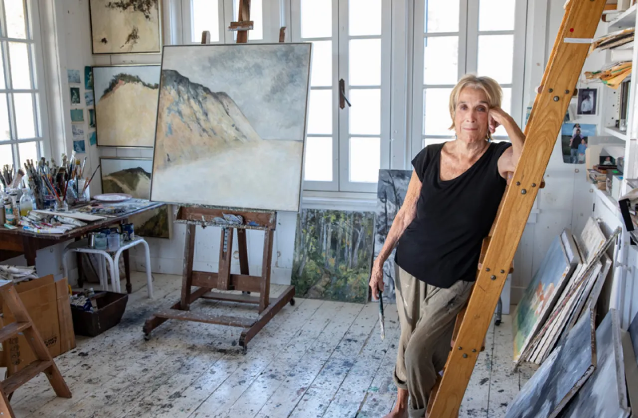 Barefoot Anne Peretz in her studio, surrounded by paintings and easels