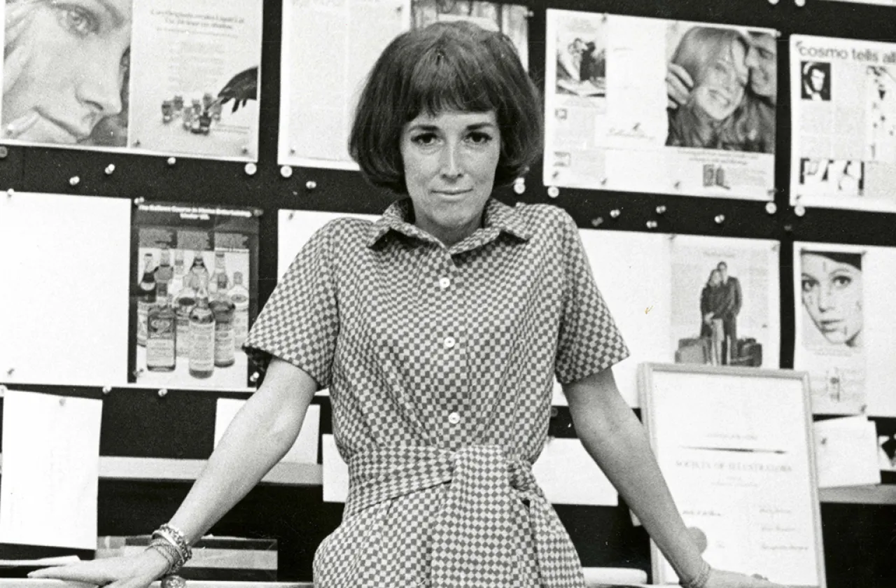 Helen Gurley Brown leaning against desk