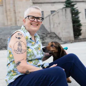 Melissa Homestead sits outside, smiling, with a dog sitting with her.