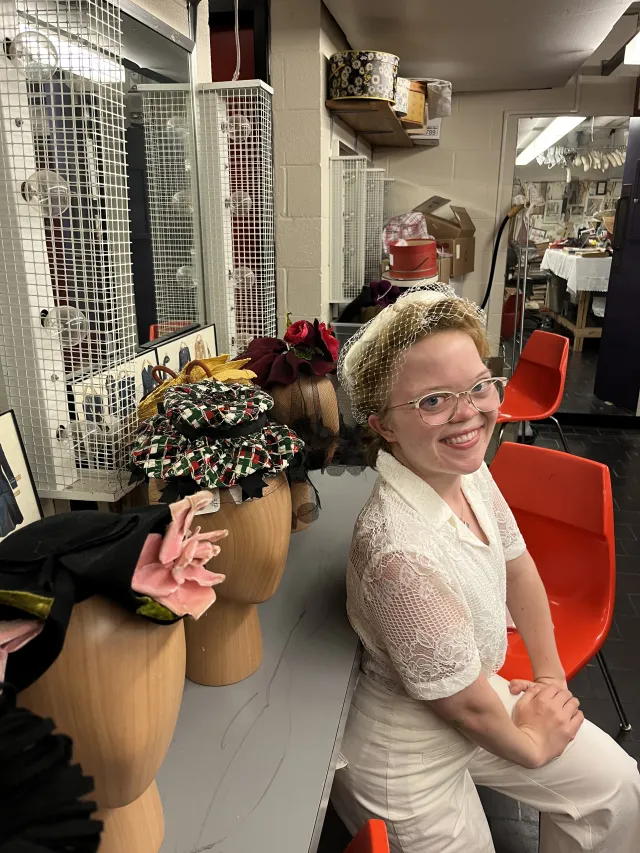 Photo of Emma O’Neill-Dietel ’22, leaning near a table that holds women's historic headpieces.