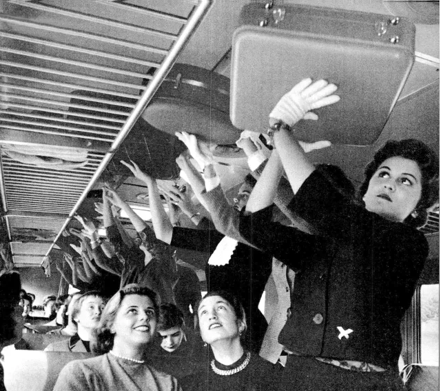 Students in 1958 lifting luggage into overhead bins on a bus.