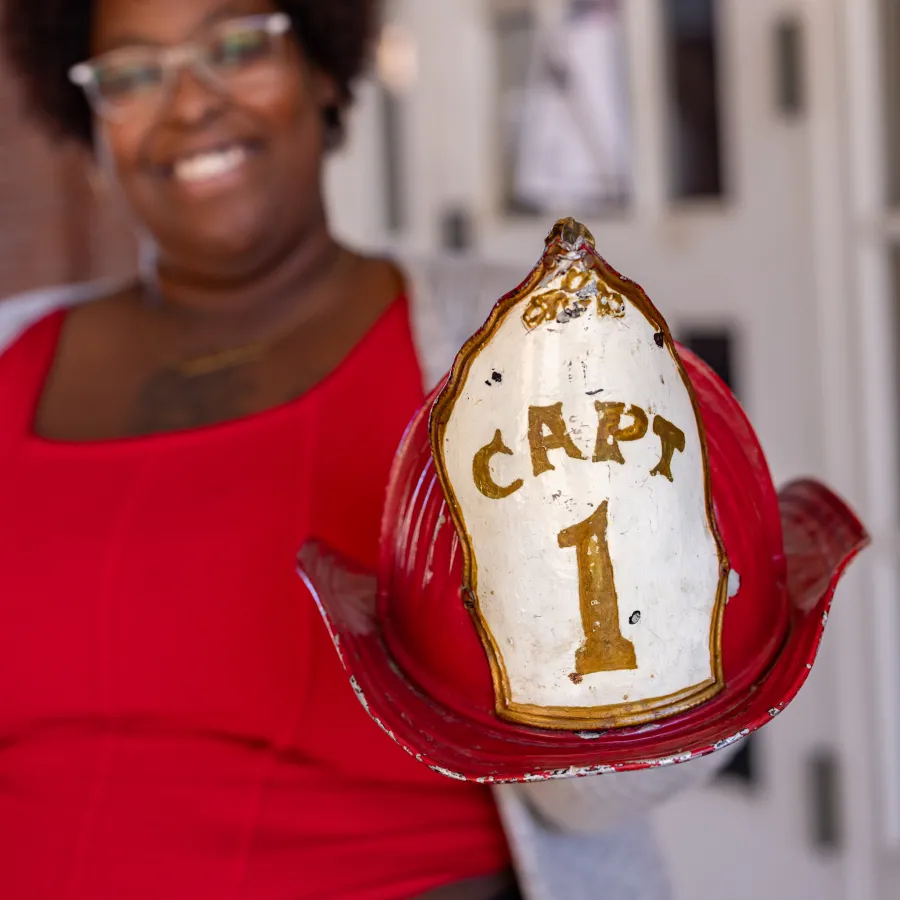 Diamond Jones holds forward an antique red fire hemet with the words Captain 1