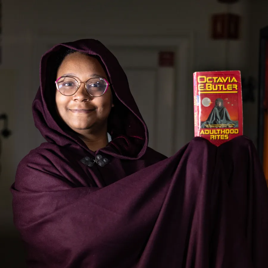 Anne-Marie Martin wears a dark cloak and holds up a copy of an Octavia Butler book.