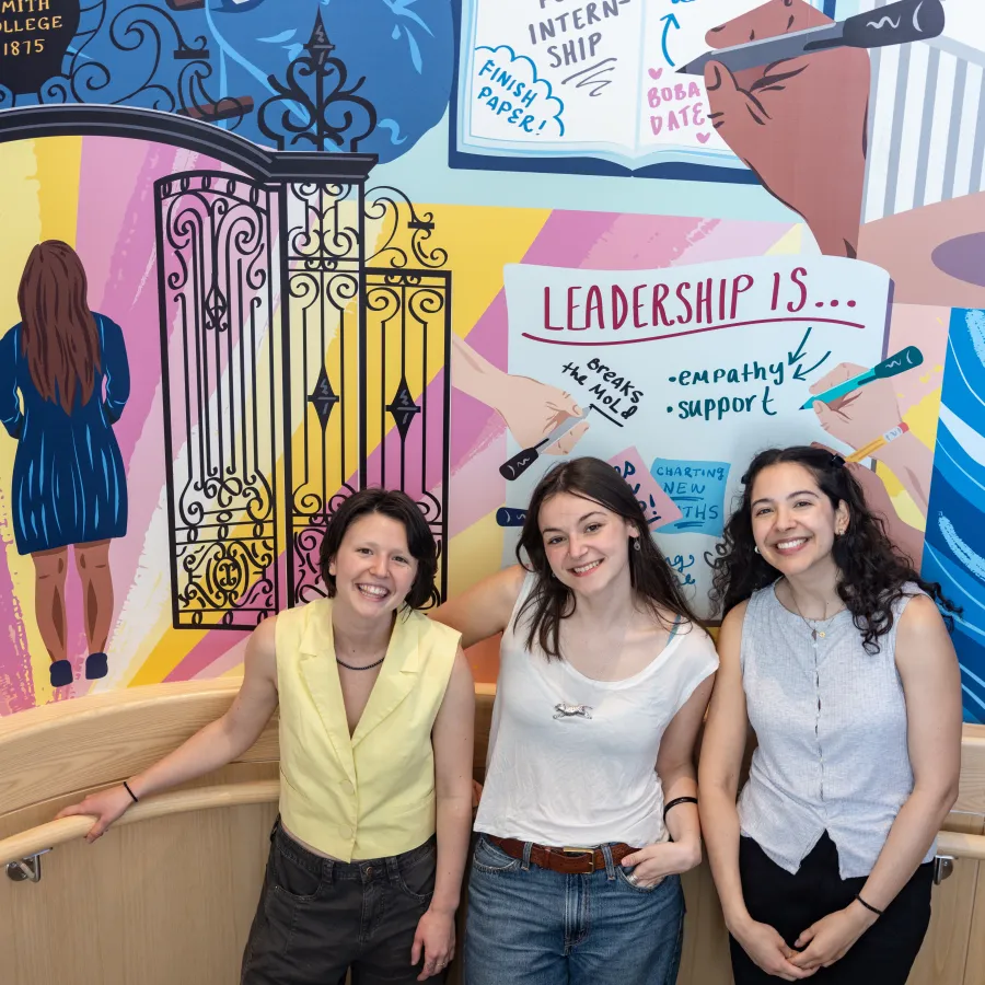 Three people stand in front of a colorful mural.