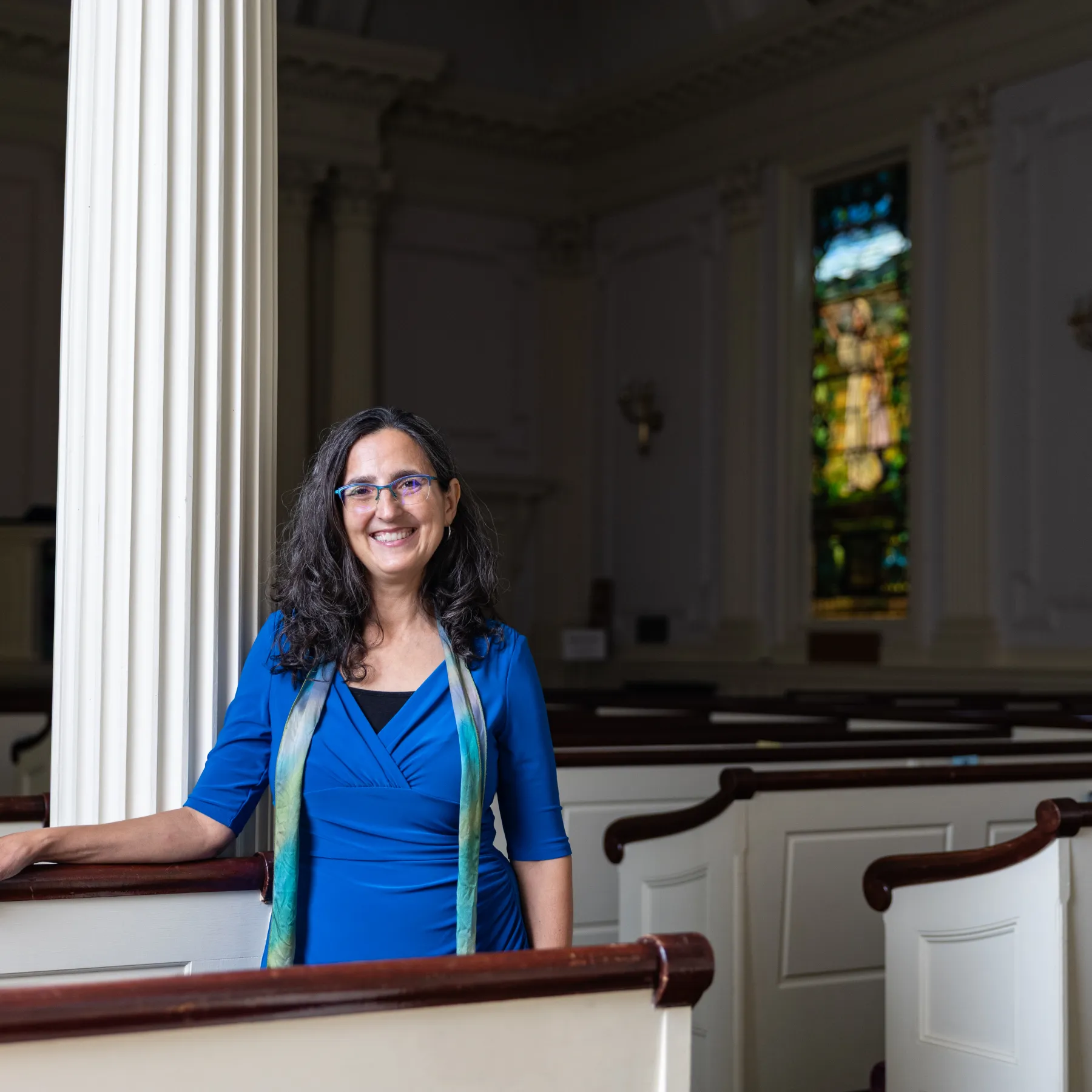 The Rev. Melissa Carvill Zeimer leans against a pew at the Unitarian church where she is pastor