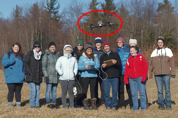 Group of students facing camera with drone hovering above