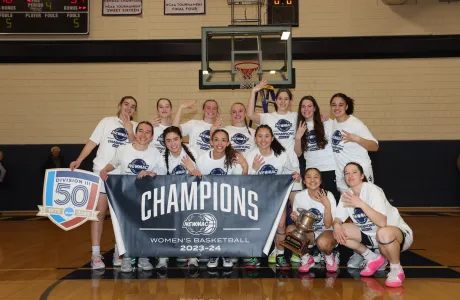 The 2023-2024 basketball team posing with their NEWMAC championship banner.