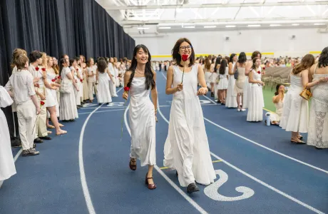 Two seniors hold roses and walk on the indoor track during Ivy Day