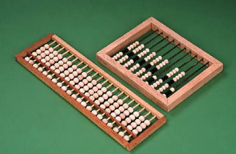 Two wooden abacuses. The left one is laid horizontally with white beads, while the right one is square-shaped with columns of white and black beads.