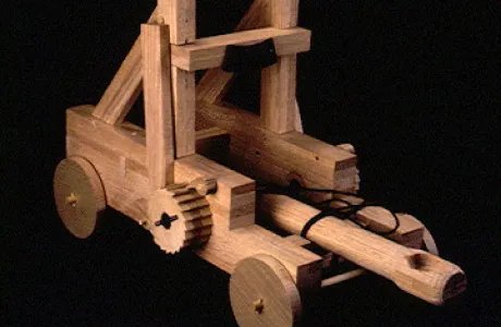 A wooden model catapult features detailed gears, wheels, and a launching arm