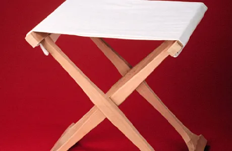 A wooden folding stool with a white cloth seat and legs that form an "X" shape