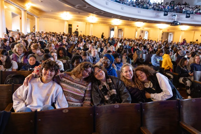 A group of five students smile for the camera, surrounded by many other students in attendance at Cromwell Day, all seated in the auditorium.