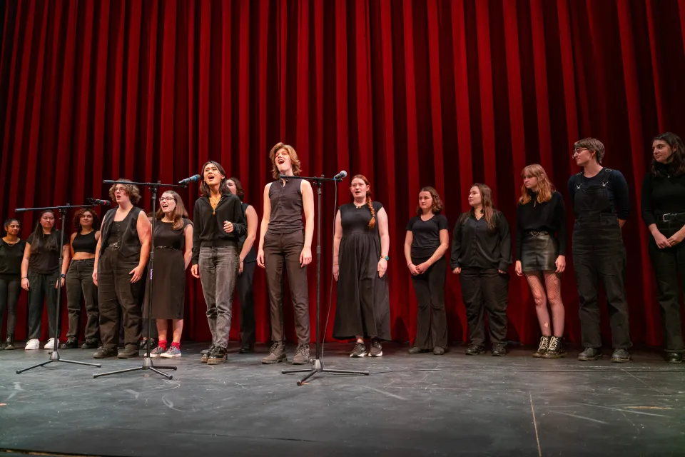A group of Smith students singing in front of a red curtain