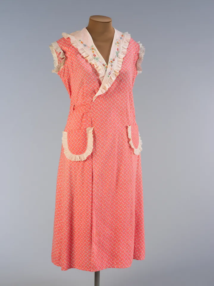 Coral-colored, sleeveless wrap dress with a large lapel and two large pockets on the front.