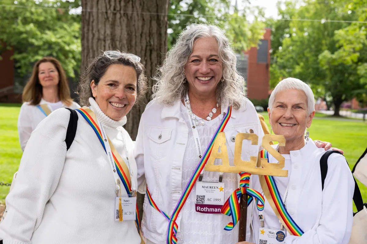 Ada Comstock Scholar alums wear white with rainbow-colored sashes and smile at the camera during Reunion