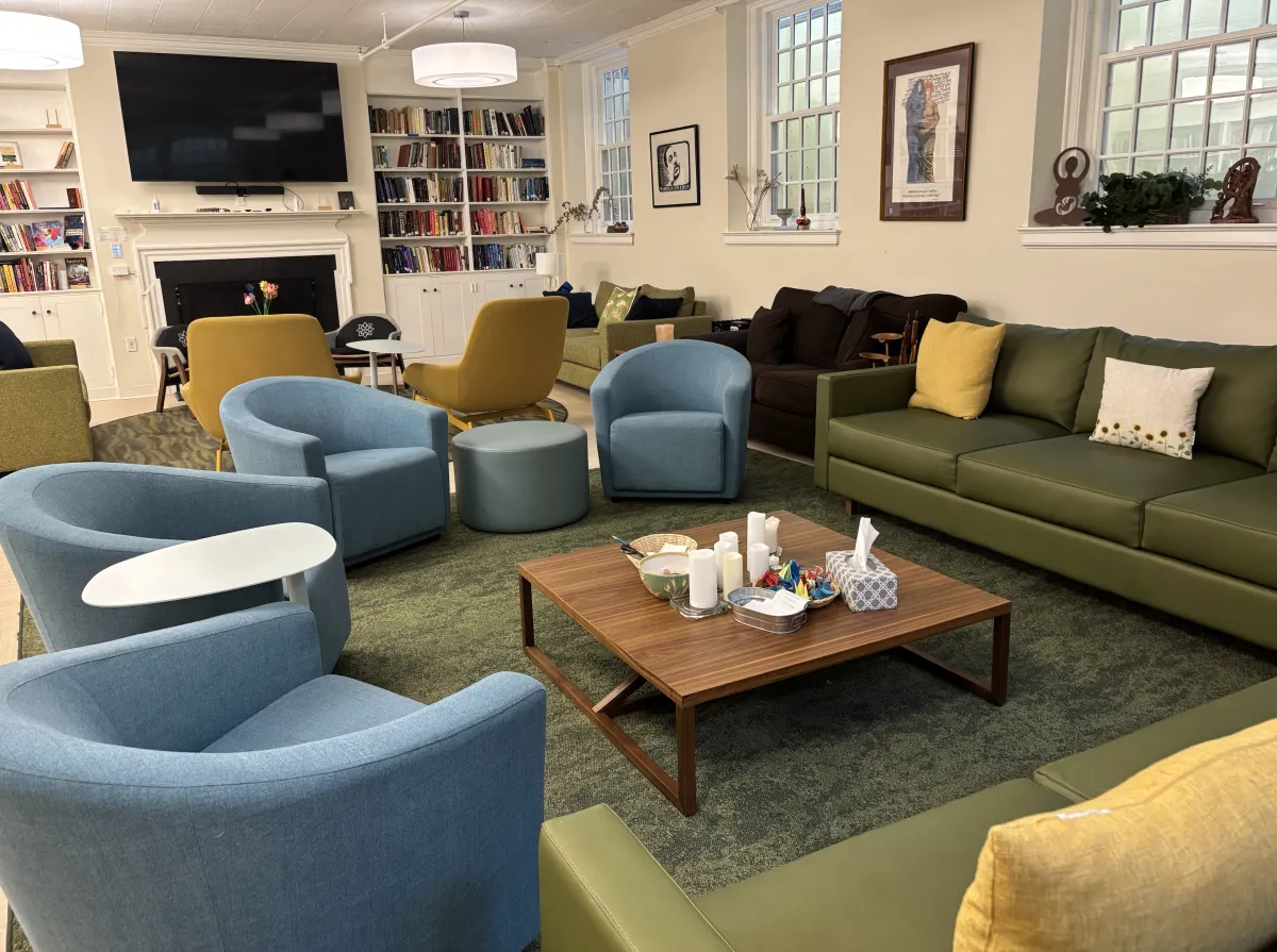 The Bodman lounge in the chapel, featuring a large TV, fireplace, comfortable chairs and sofas, and a large bookshelf.
