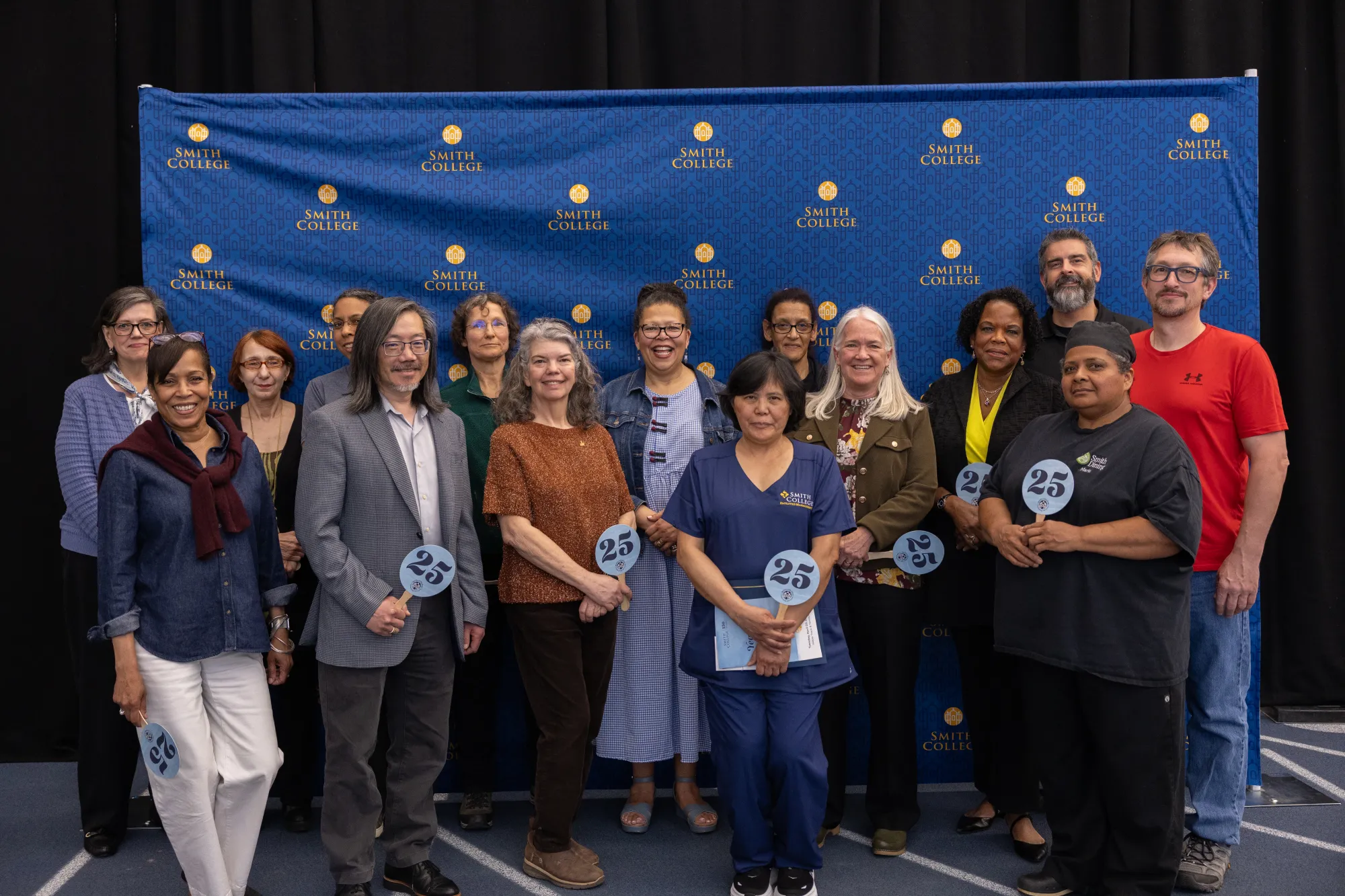 A group of employees holding signs that say "25" in front of a Smith College backdrop during the 2025 Years of Service reception