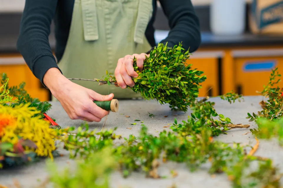 Julie Thomson's hands as she winds green wire around a wreath ring and evergreen bundle