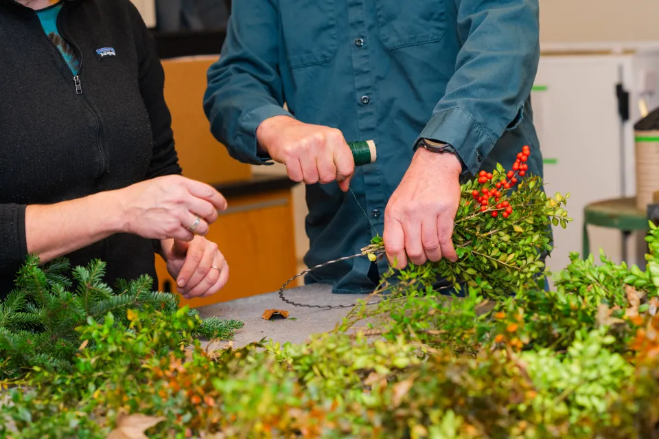 Dave Dion's and Julie Thomson's hands as they winds green wire around a wreath ring