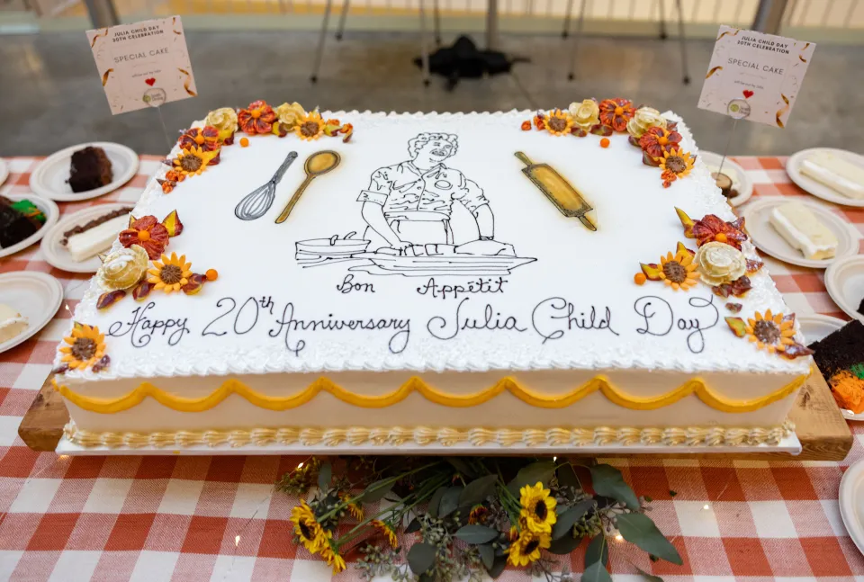 A cake decorated with flowers, an image of Julia Child, and text that reads "Bon Appétit, Happy 20th Anniversary Julia Child Day"