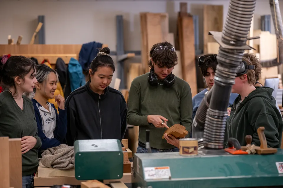 A group of students examines a block of wood in the Hillyer Hall Woodshop during an interterm class