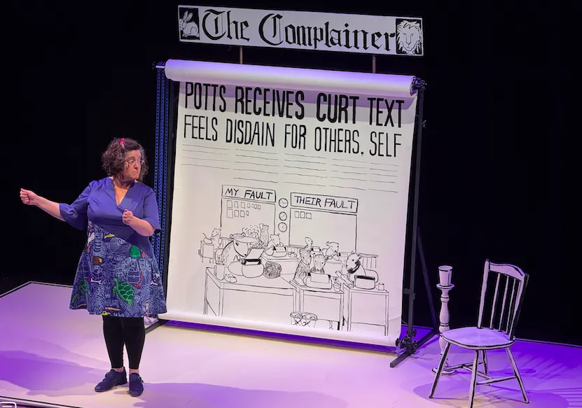 Phoebe Potts on stage during a performance of Too Fat For China. A giant fake newspaper is behind her.