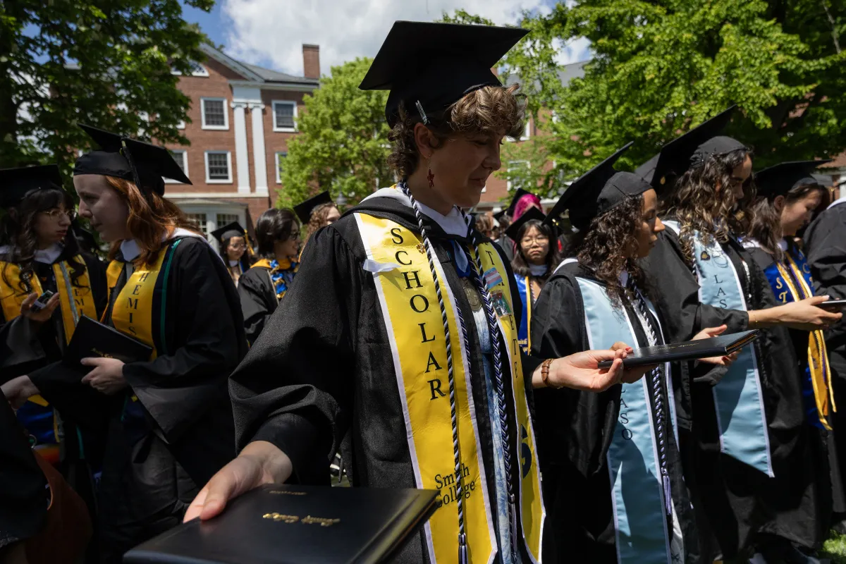 Students smile while passing diplomas in a circle after Commencement