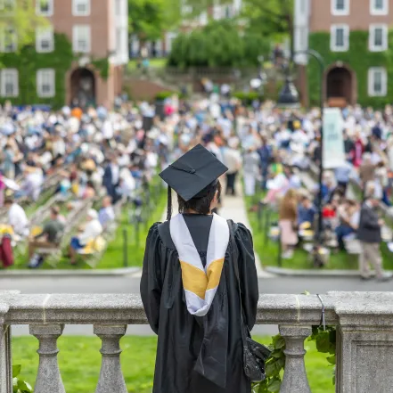 A senior in cap and gown faces away from the camera, looking out into the Quad on Commencement Day