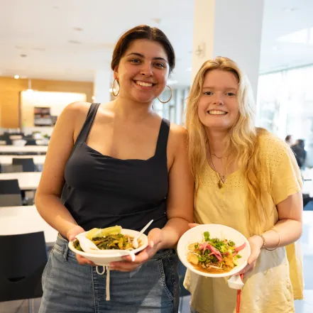 Two students holding bowls of food during a pop-up plant-based event