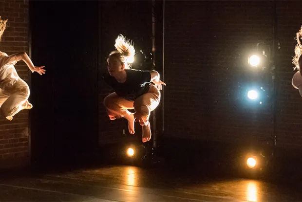 Three dancers mid-air in front of brick backdrops